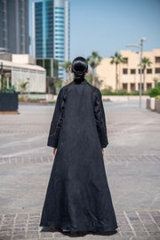 Back view of woman wearing modern black Velora abaya with brown linen details and wide lapels in urban setting