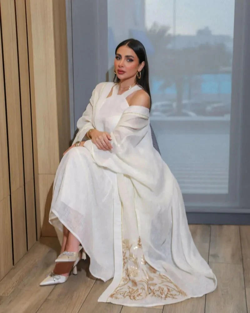 woman wearing lightweight white inner dress with long sheer embroidered outer layer sitting indoors
