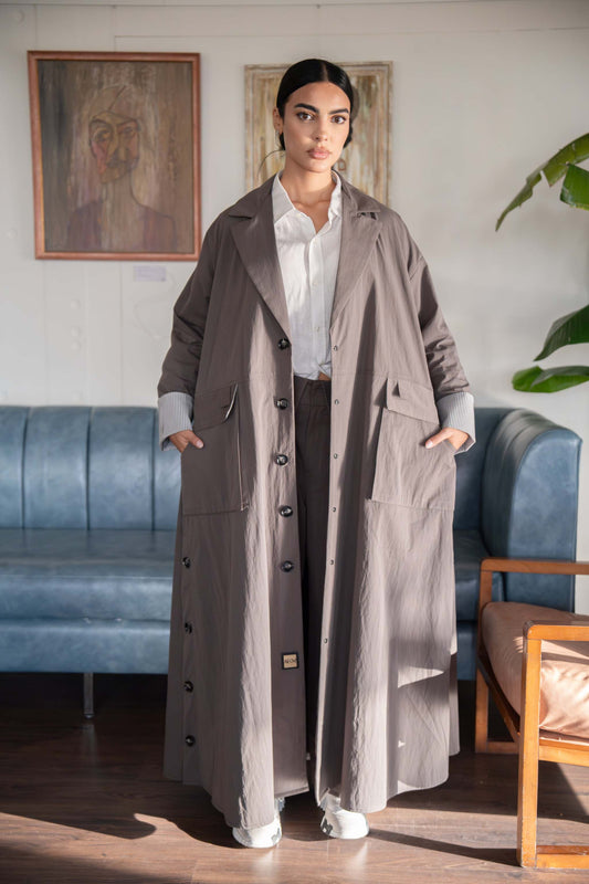 Woman wearing taupe button-down utility abaya with front buttons and side pockets in a modern living room setting