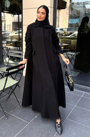 Woman wearing a black abaya with a straight cut and holding a handbag outdoors