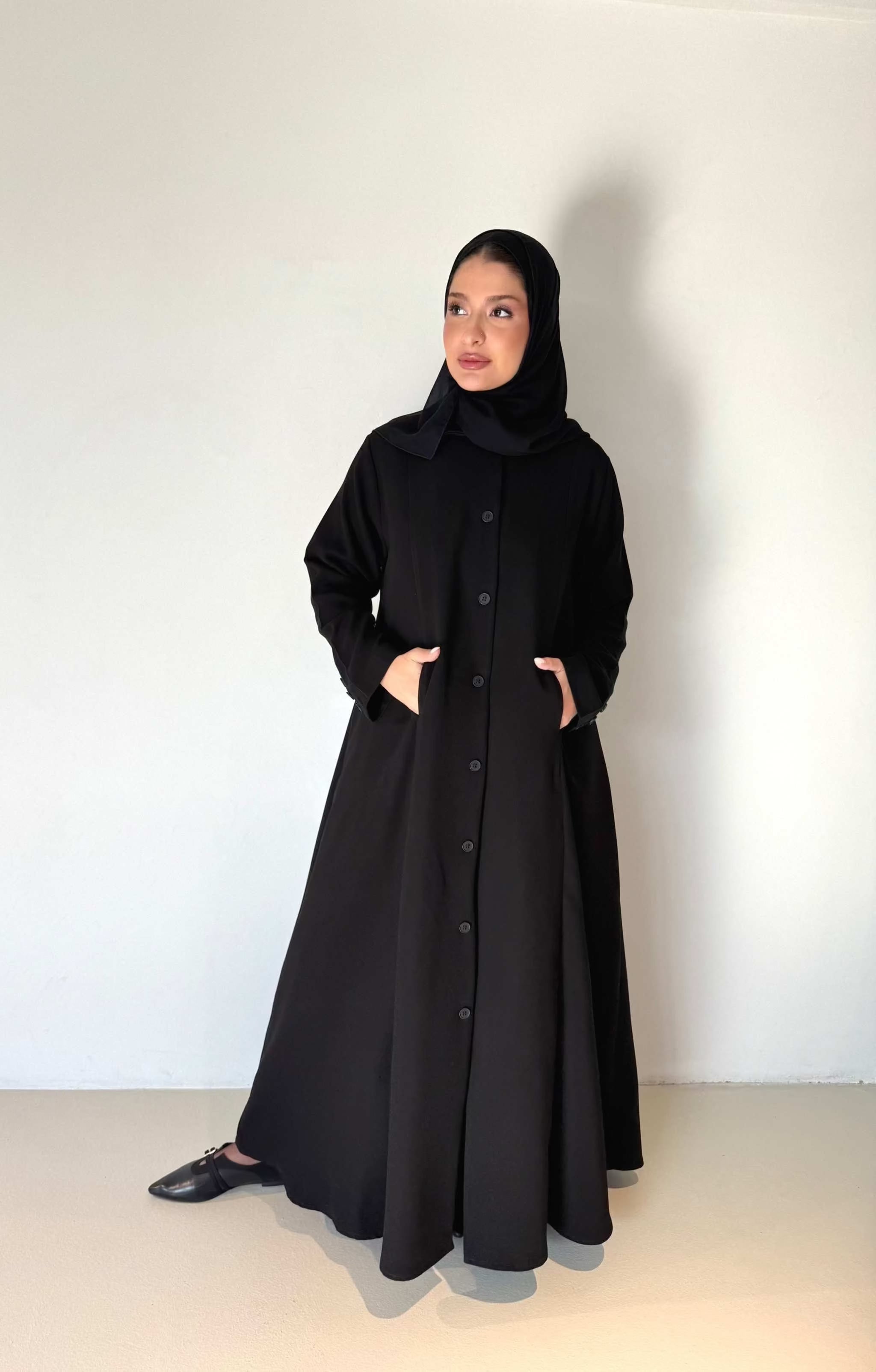 Elegant black crepe abaya with button-down front and subtle pleated skirt detail, worn with a black hijab - The Sophisticated Crepe Abaya