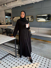 Elegant black crepe abaya with button-down front and subtle pleated skirt detail, worn with a black hijab - The Sophisticated Crepe Abaya