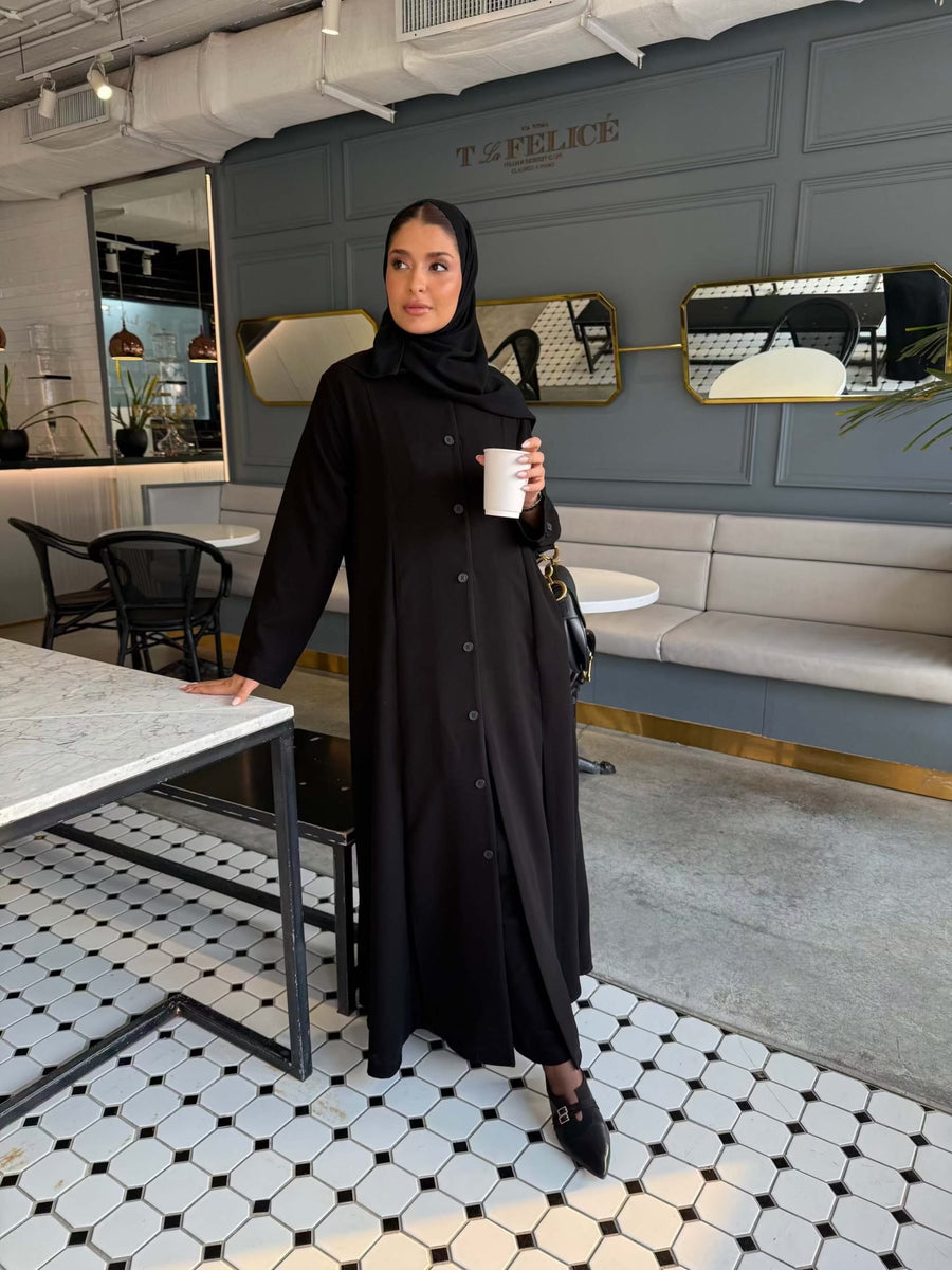 Elegant black crepe abaya with button-down front and subtle pleated skirt detail, worn with a black hijab - The Sophisticated Crepe Abaya