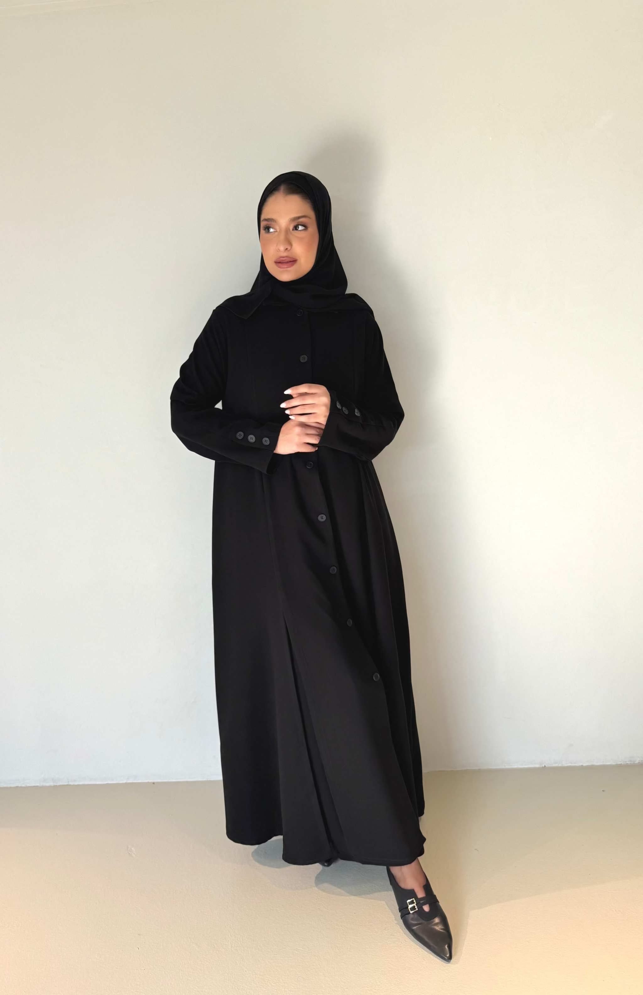 Woman wearing elegant black button-down crepe abaya with tailored fit and subtle flare at hem