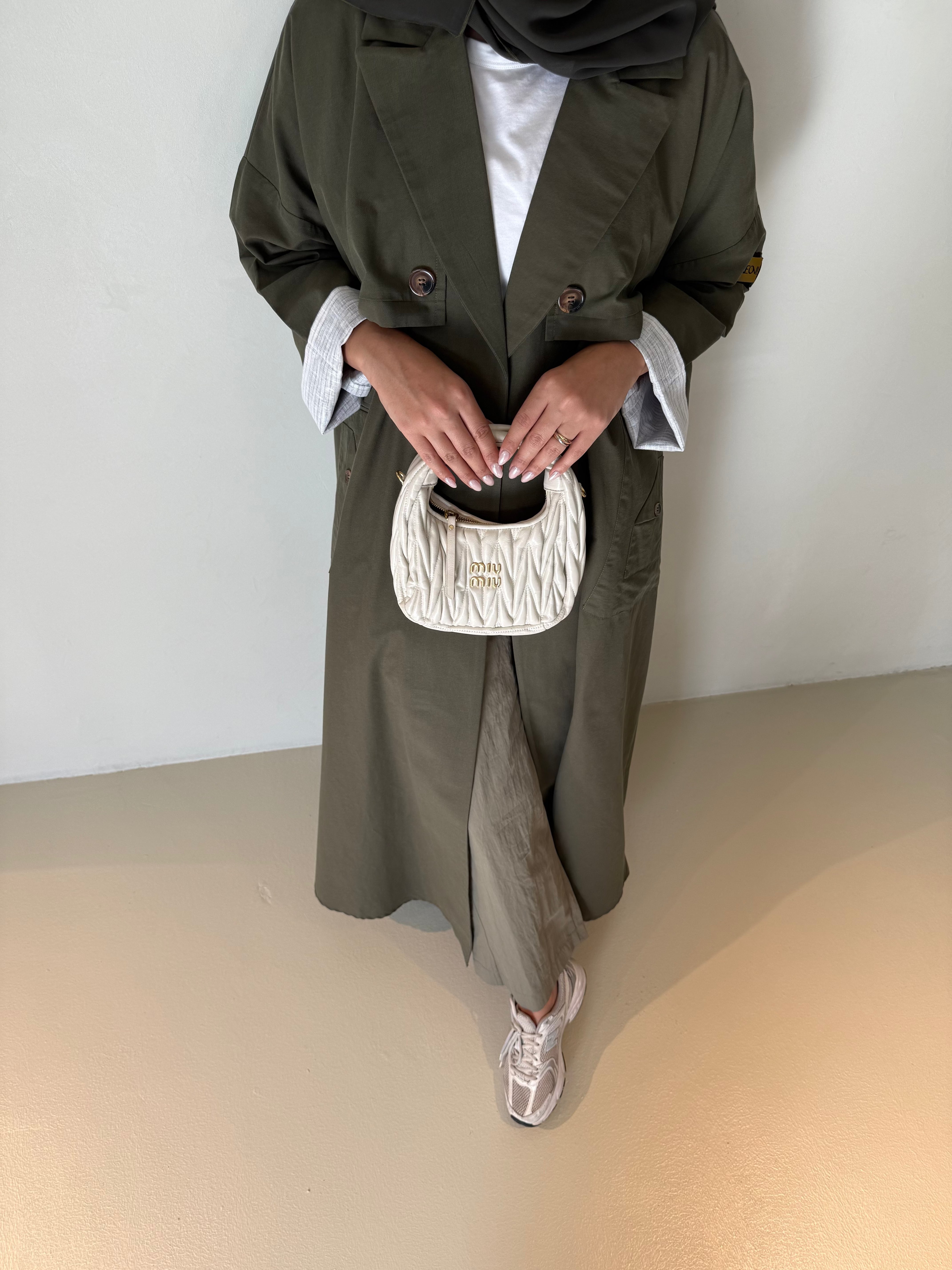 Khaki crepe wide-leg pants styled with a long coat, white top, and sneakers, accessorized with a small white handbag.