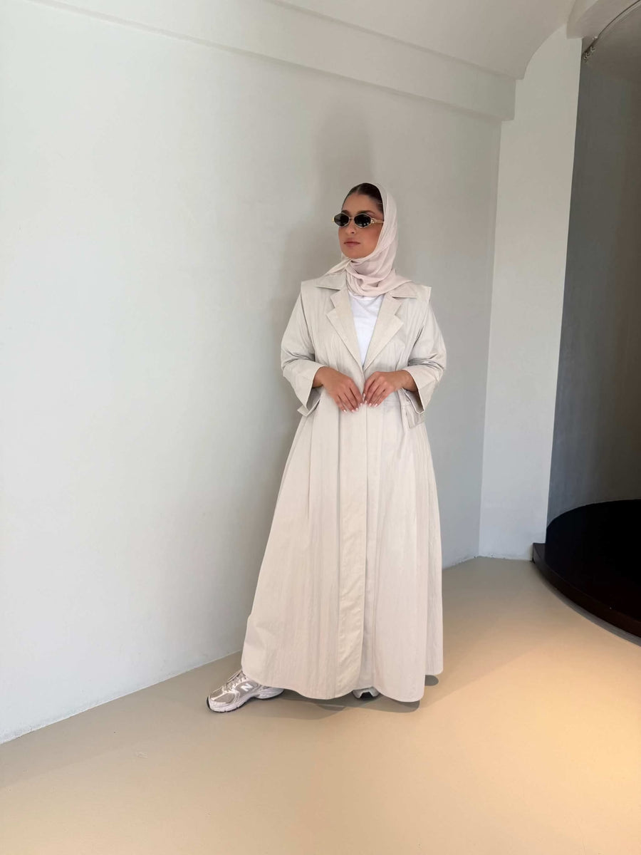 Woman wearing modern everyday beige trenchcoat with minimalist design and flowing lines standing indoors