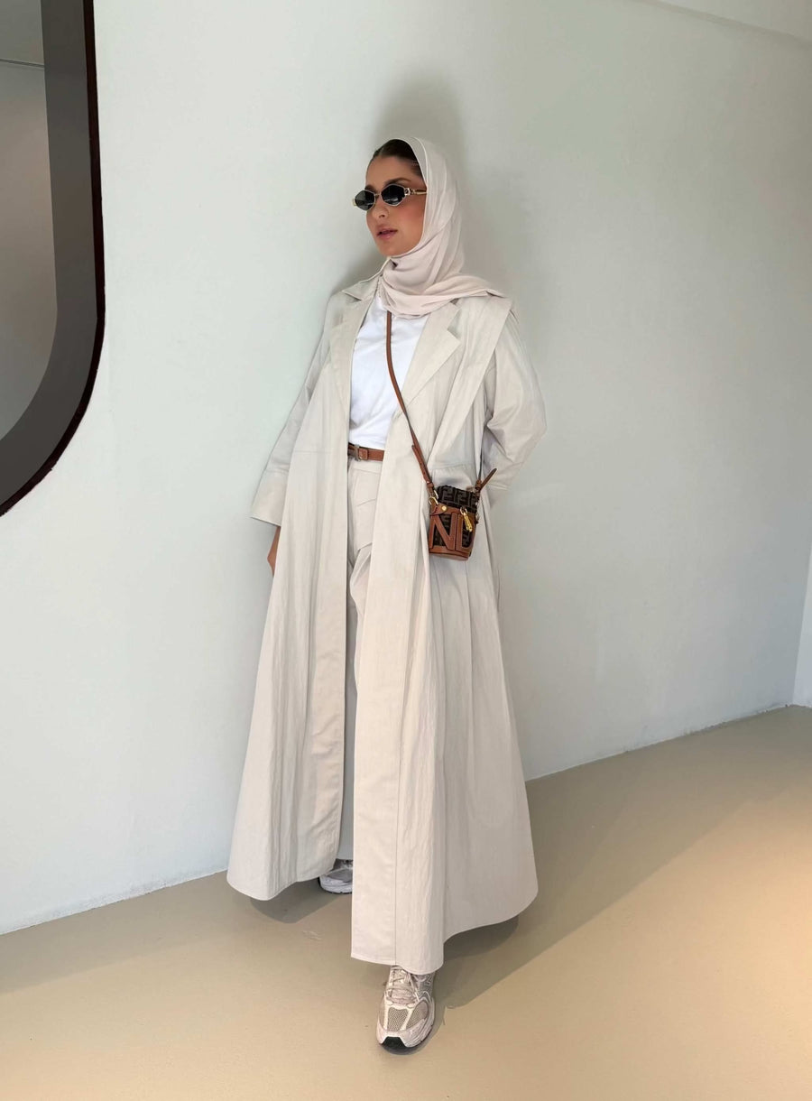 Woman wearing modern everyday beige trenchcoat with minimalist design and flowing lines standing indoors