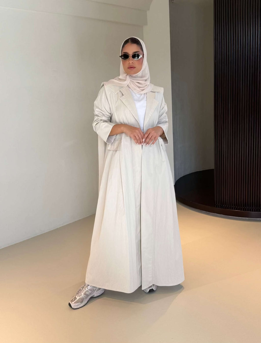Woman wearing modern everyday beige trenchcoat with minimalist design and flowing lines standing indoors