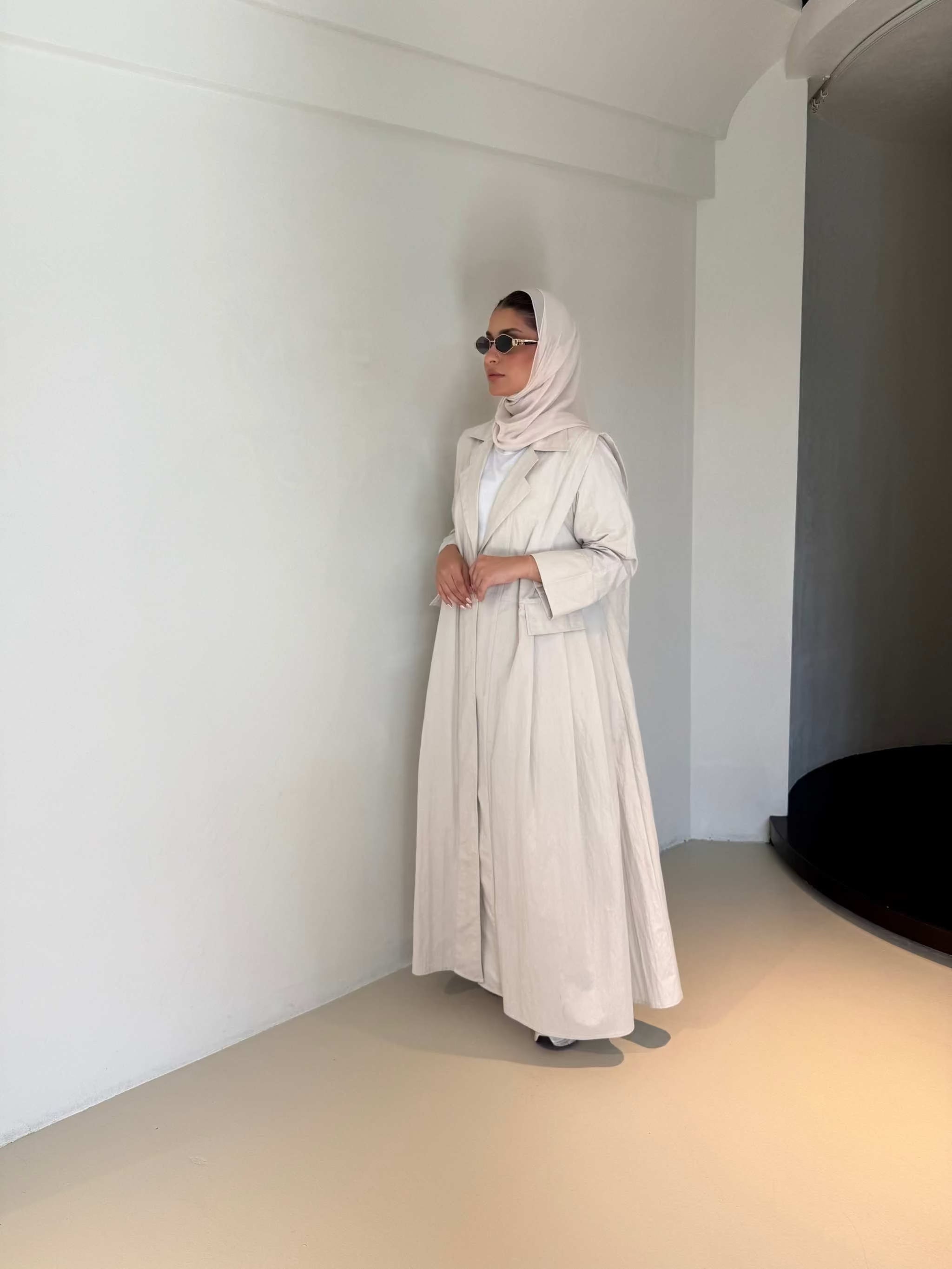 Woman wearing modern everyday beige trenchcoat with minimalist design and flowing lines standing indoors