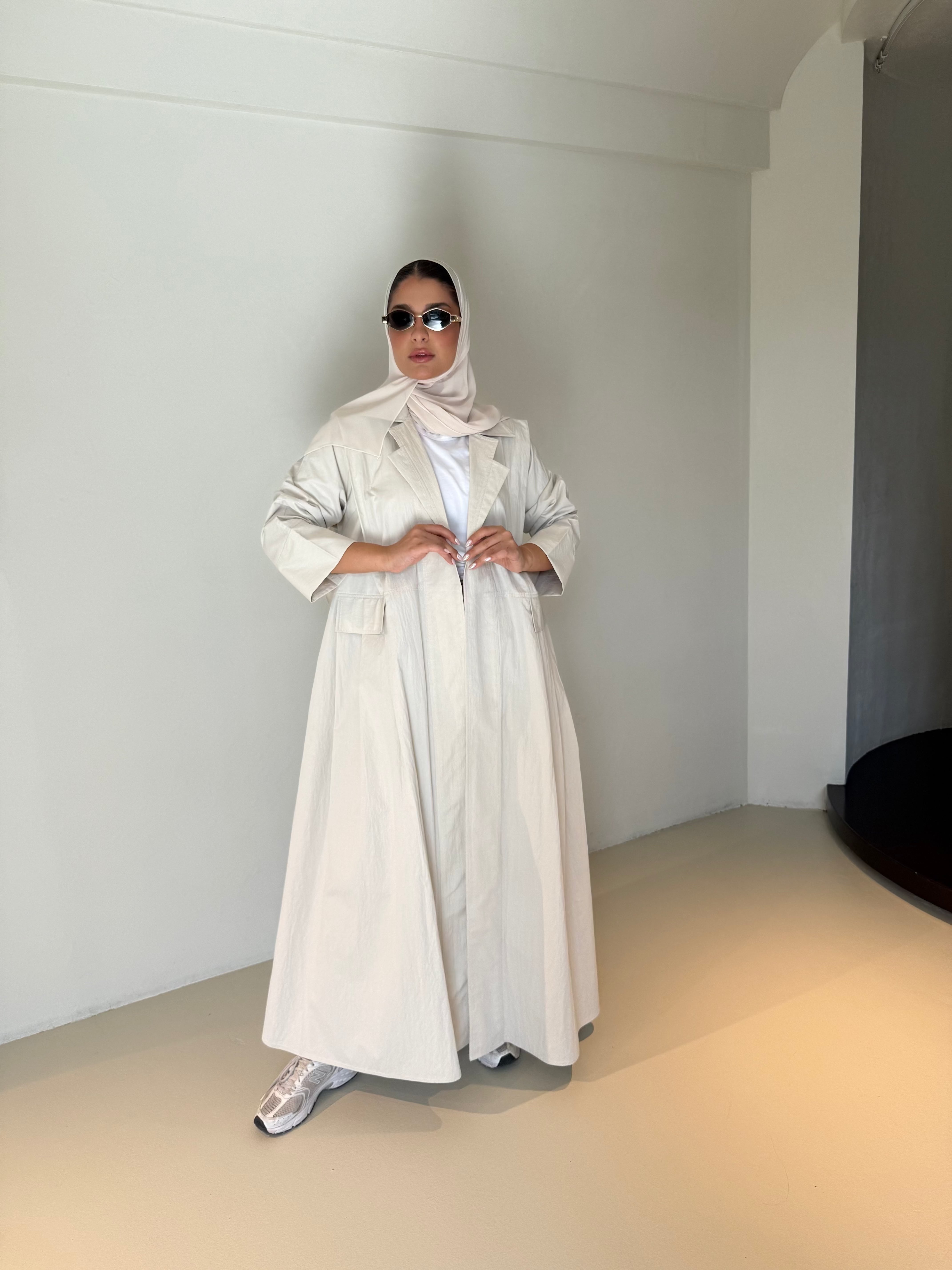 Woman wearing modern everyday beige trenchcoat with minimalist design and flowing lines standing indoors