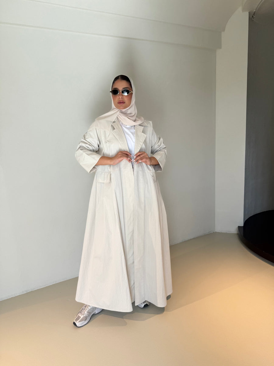 Woman wearing modern everyday beige trenchcoat with minimalist design and flowing lines standing indoors