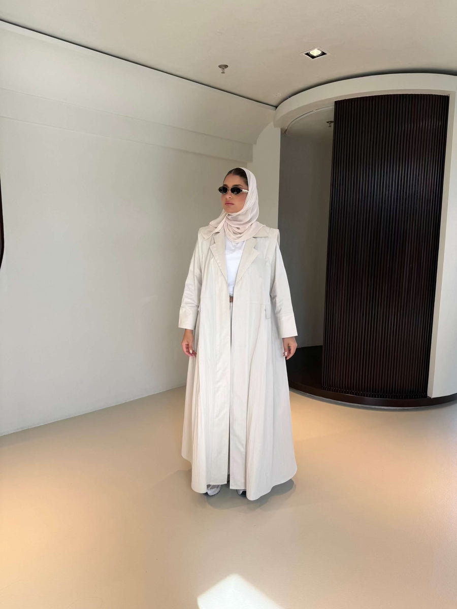 Woman wearing modern everyday beige trenchcoat with minimalist design and flowing lines standing indoors