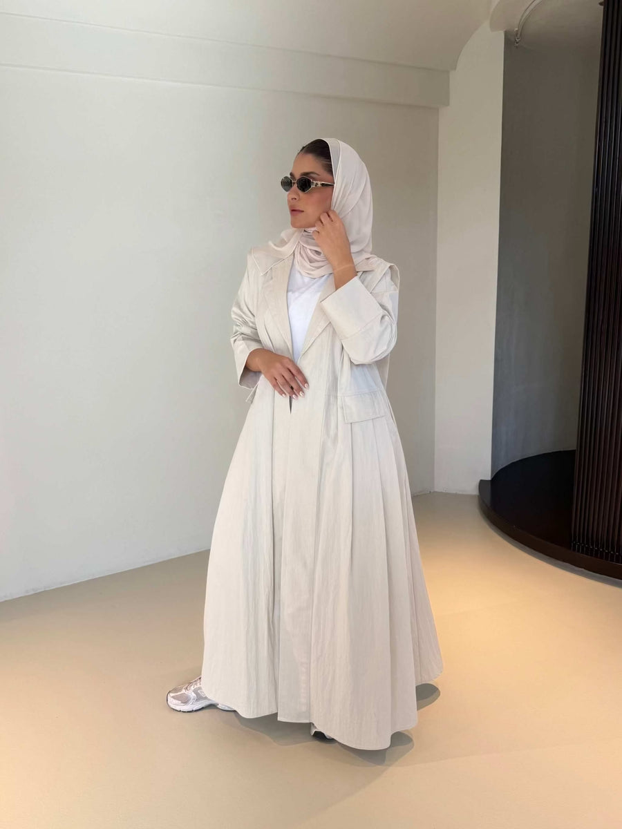 Woman wearing modern everyday beige trenchcoat with minimalist design and flowing lines standing indoors