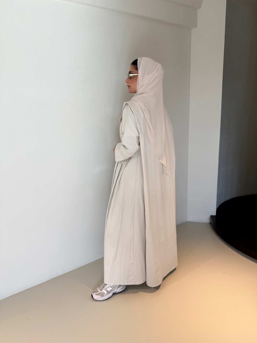 Woman wearing modern everyday beige trenchcoat with minimalist design and flowing lines standing indoors