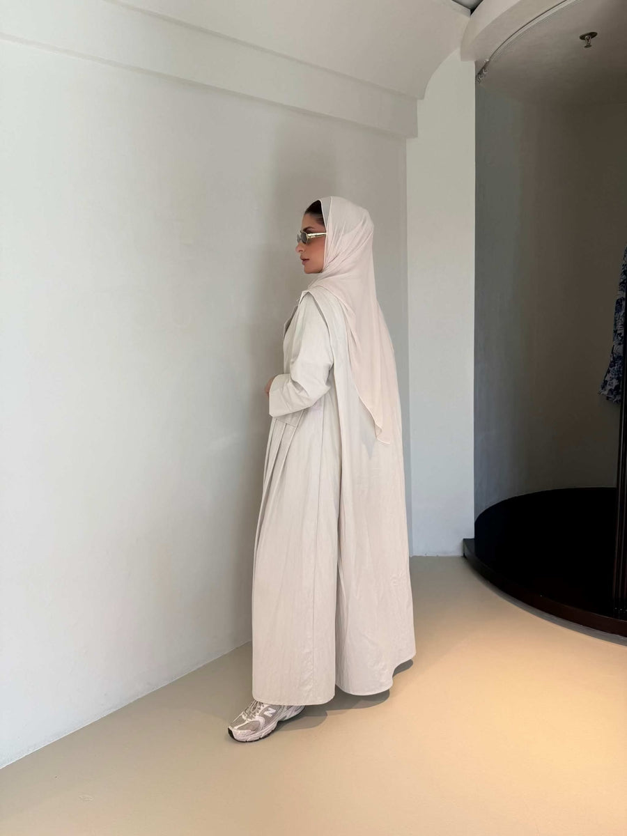 Woman wearing modern everyday beige trenchcoat with minimalist design and flowing lines standing indoors