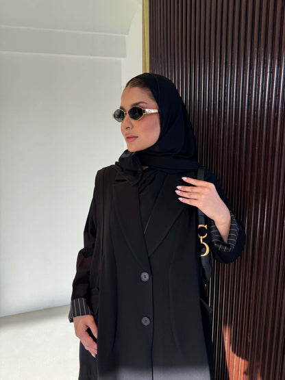 Black crepe trench abaya with striped cuff detailing and pleated skirt silhouette worn with black hijab and sunglasses