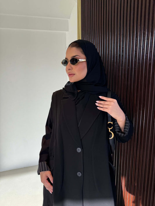 Black crepe trench abaya with striped cuff detailing and pleated skirt silhouette worn with black hijab and sunglasses