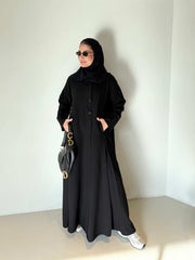 Black flowing crepe abaya with full button-down front, lightweight and elegant, styled with a black hijab and sunglasses.