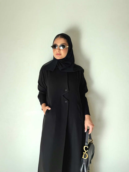 Black flowing crepe abaya with full button-down front, lightweight and elegant, styled with a black hijab and sunglasses.