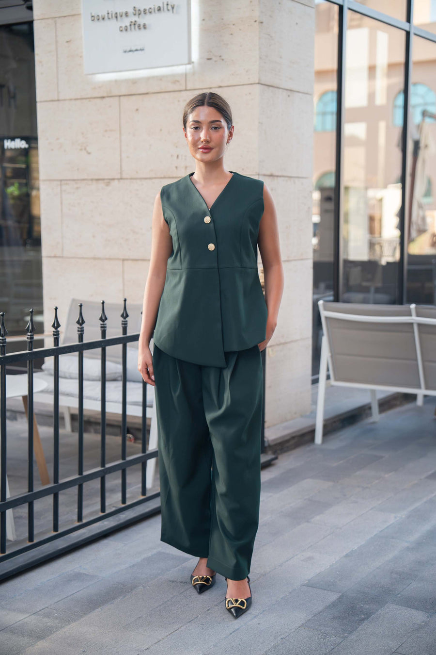 woman wearing emerald green sleeveless top with gold buttons and matching trousers standing outdoors