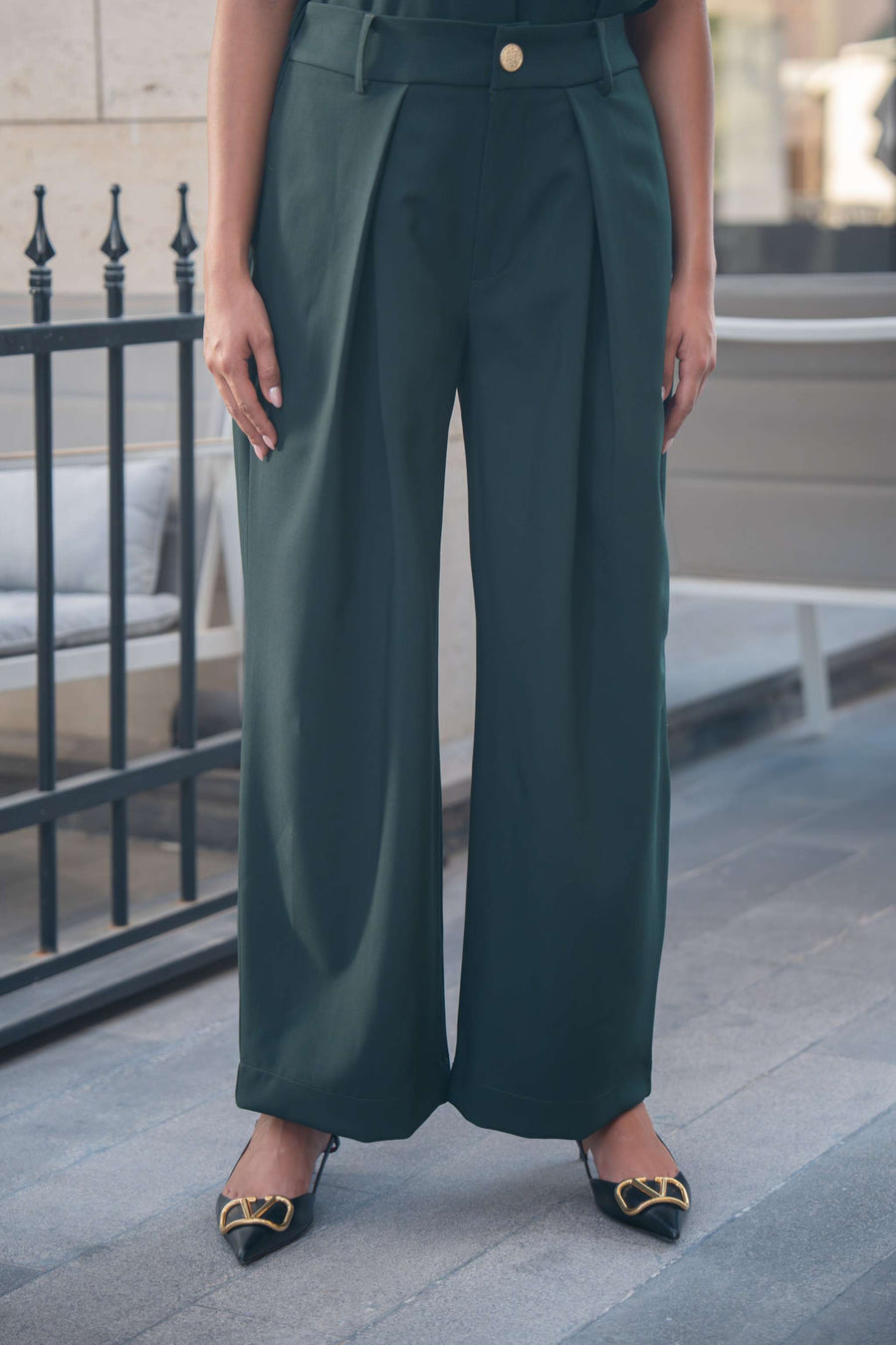 Emerald green wide-leg tailored trousers with sharp pleats and gold button detail.