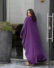 Woman wearing a flowing purple abaya made of shimmering silk standing outdoors near a door.