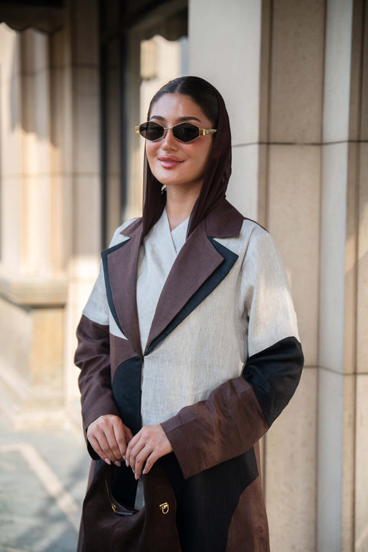 Woman wearing a two-tone linen abaya with brown, beige, and black contrast panels and tailored lapel collar outdoors