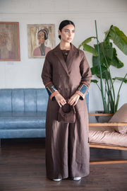 Woman wearing long brown coat with embroidered cuffs holding matching bag indoors 834