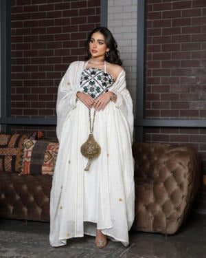 Woman wearing a graceful Ramadan set with white linen bisht and gold embroidery, holding a decorative handbag.
