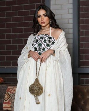 Woman wearing a graceful Ramadan set with white linen bisht and gold embroidery, holding a decorative handbag.