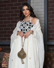 Woman wearing a graceful Ramadan set with white linen bisht and gold embroidery, holding a decorative handbag.