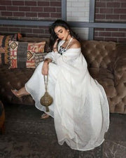 Woman wearing a graceful Ramadan set with white linen bisht and gold embroidery, holding a decorative handbag.