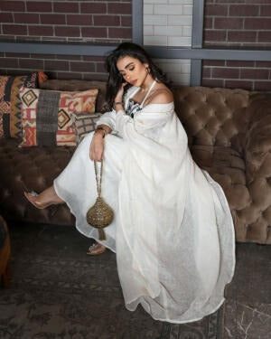 Woman wearing a graceful Ramadan set with white linen bisht and gold embroidery, holding a decorative handbag.