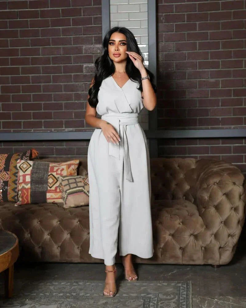 woman wearing sleeveless grey jumpsuit with wrap V-neckline and waist tie standing in front of brick wall