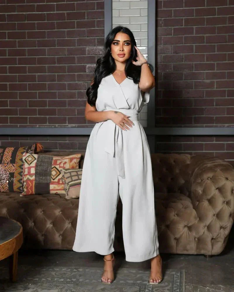 woman wearing sleeveless grey jumpsuit with wrap V-neckline and waist tie standing in front of brick wall