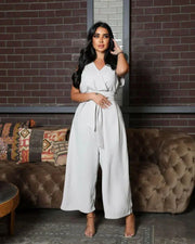 woman wearing sleeveless grey jumpsuit with wrap V-neckline and waist tie standing in front of brick wall