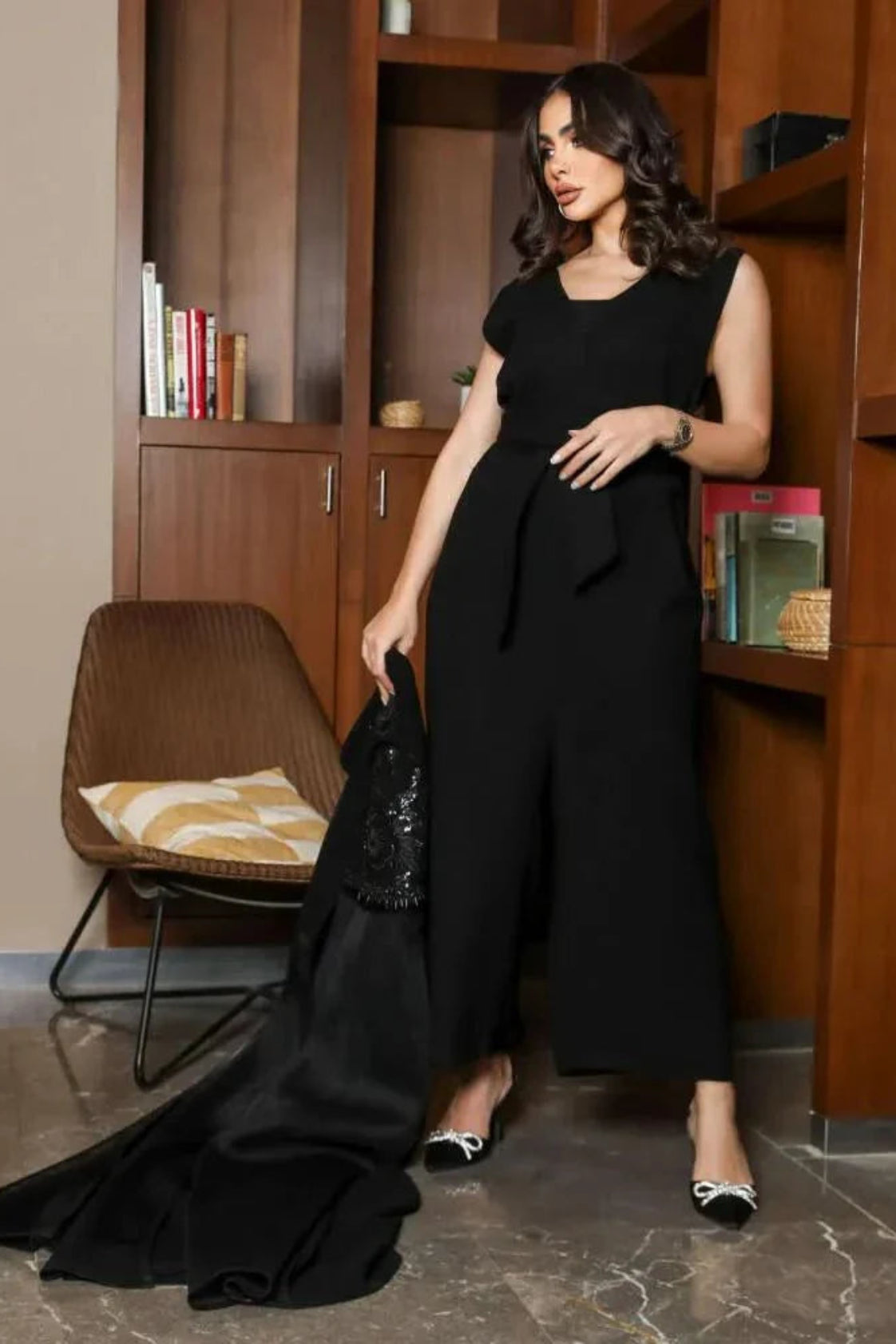Woman wearing sleeveless black jumpsuit with V-neck and waist tie standing indoors