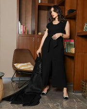 Woman wearing sleeveless black jumpsuit with V-neck and waist tie standing indoors