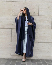Velune luxurious dark blue silk bisht flowing elegantly on a woman against a stone wall background