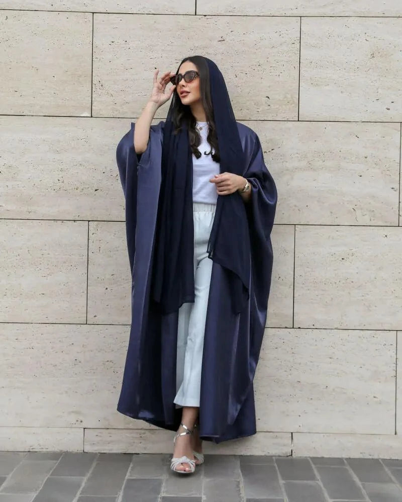 Velune luxurious dark blue silk bisht flowing elegantly on a woman against a stone wall background