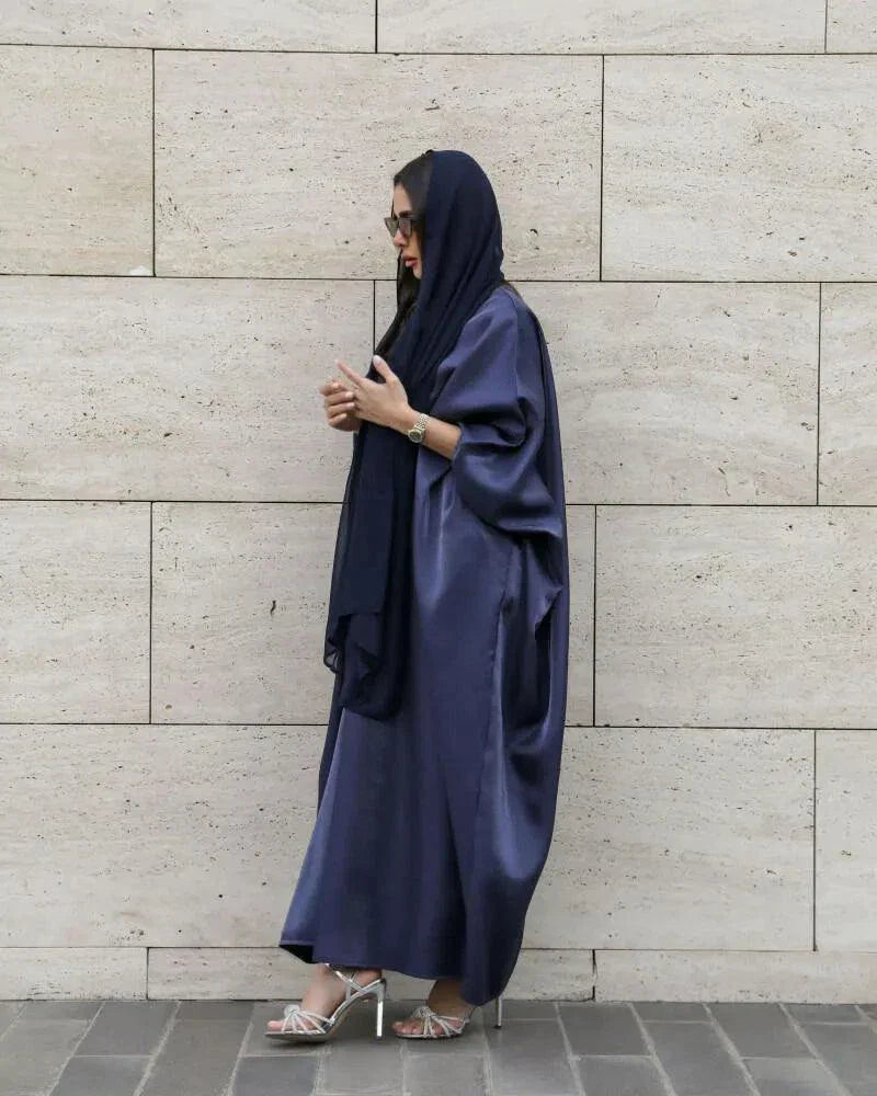 Woman wearing a rich navy abaya in shimmering silk with a classic batwing cut and matching sheila scarf.