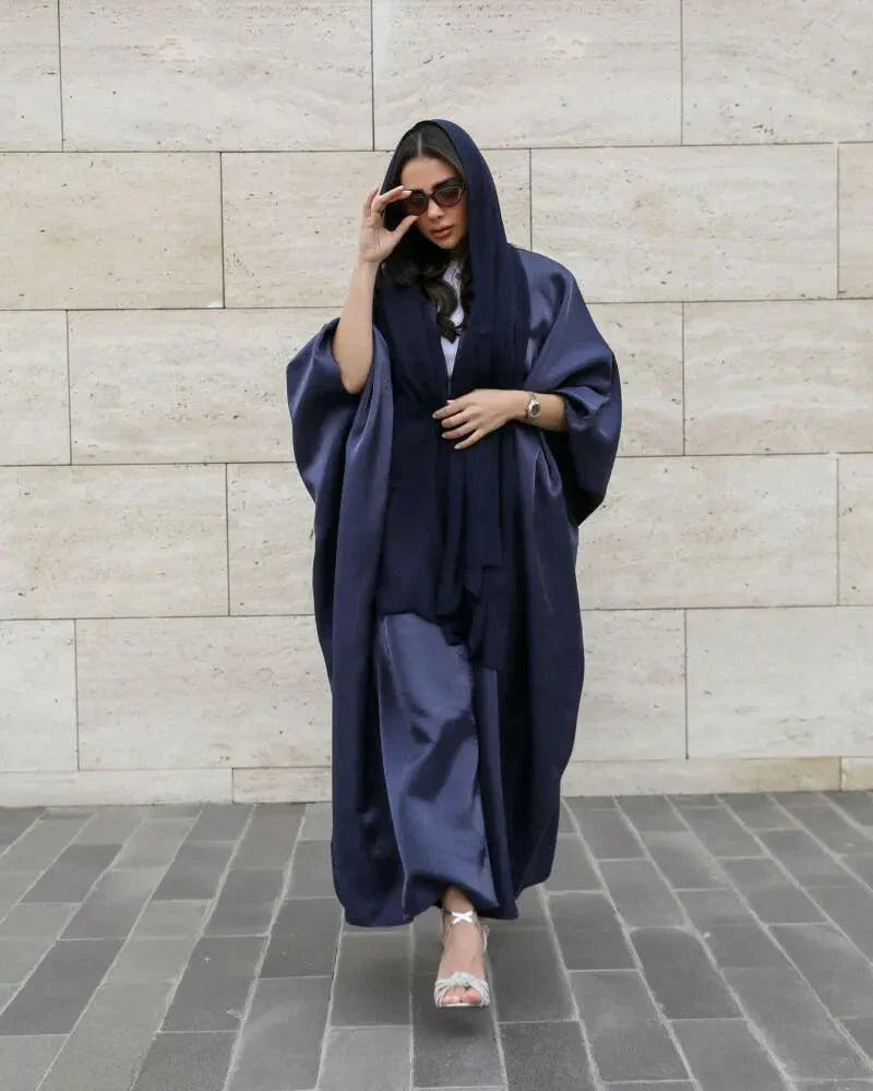 Woman wearing a shimmering rich navy abaya with a classic batwing cut and matching sheila scarf, styled with heels.