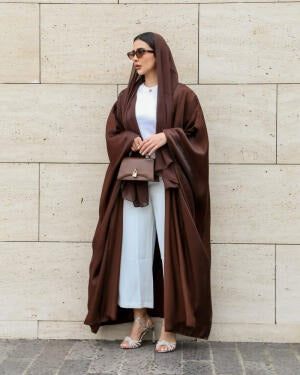 Woman wearing Serra shimmering brown silk bisht over white outfit with sunglasses and handbag.