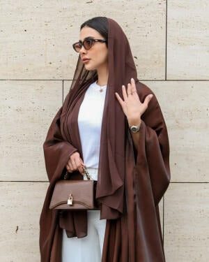 Woman wearing Serra shimmering brown silk bisht over white outfit with sunglasses and handbag.