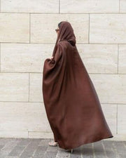 Woman wearing Serra shimmering brown silk bisht over white outfit with sunglasses and handbag.