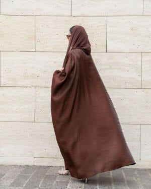 Woman wearing Serra shimmering brown silk bisht over white outfit with sunglasses and handbag.