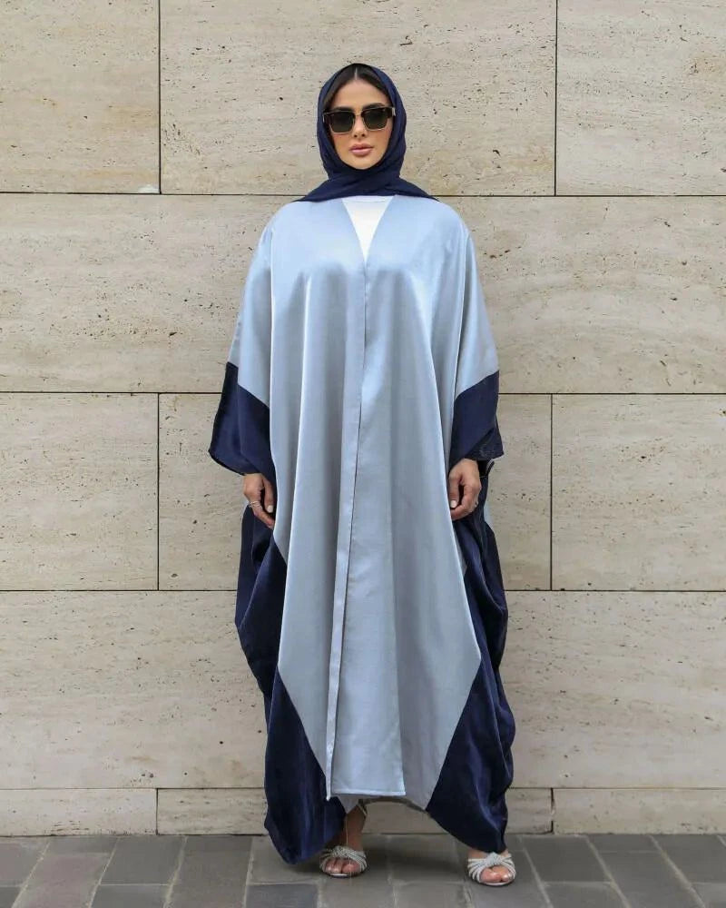 woman wearing silver and navy blue shimmering silk elegant flowy abaya with sunglasses standing against stone wall