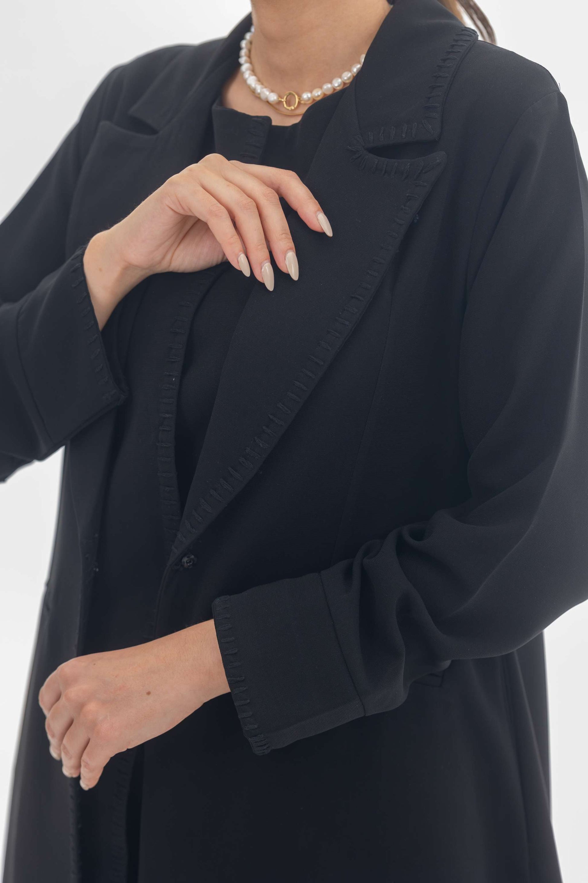 Black crepe blazer abaya with tailored silhouette and intricate black embroidery, styled with a pearl necklace.