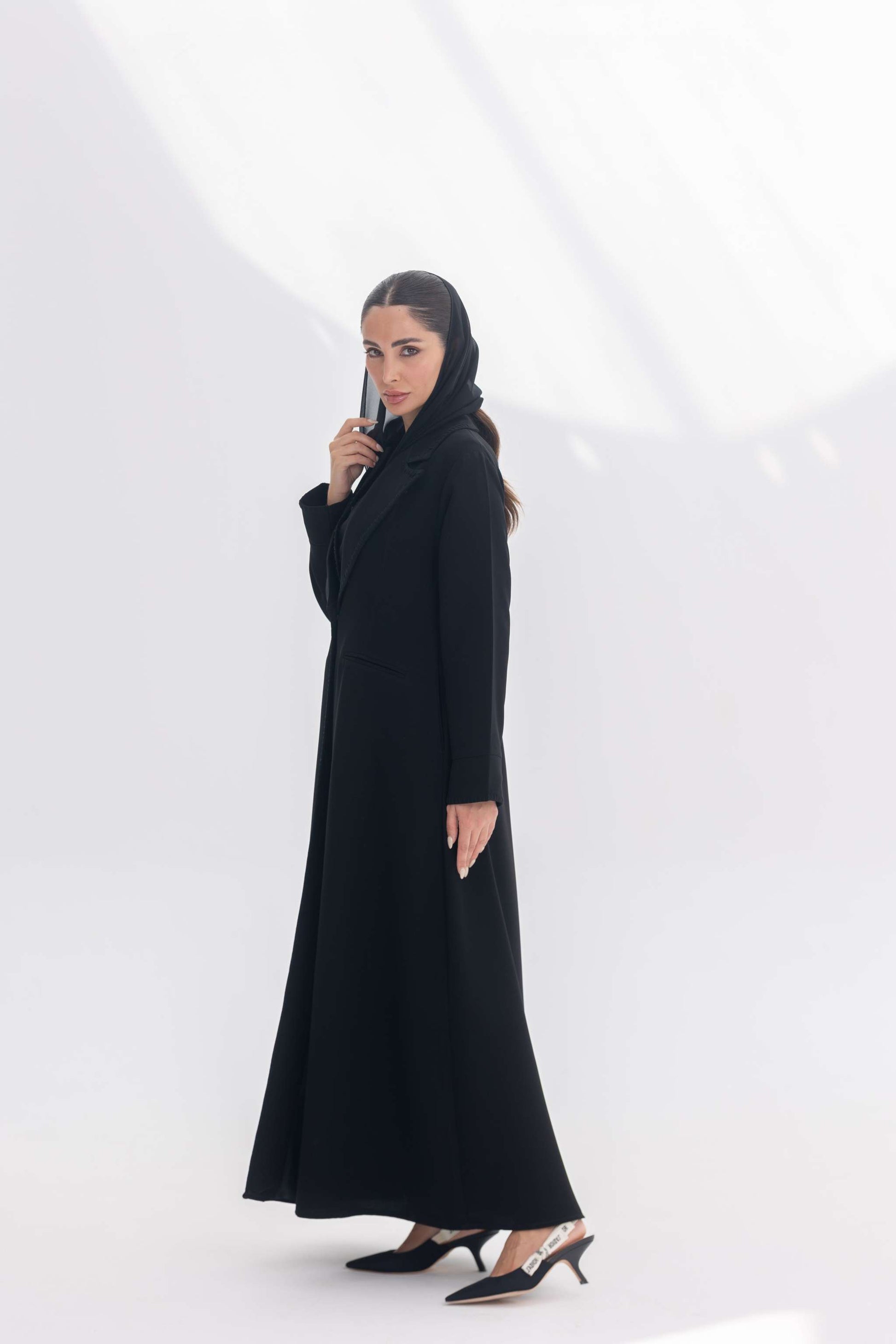 Woman wearing black crepe blazer abaya with intricate embroidery and tailored silhouette standing against white background