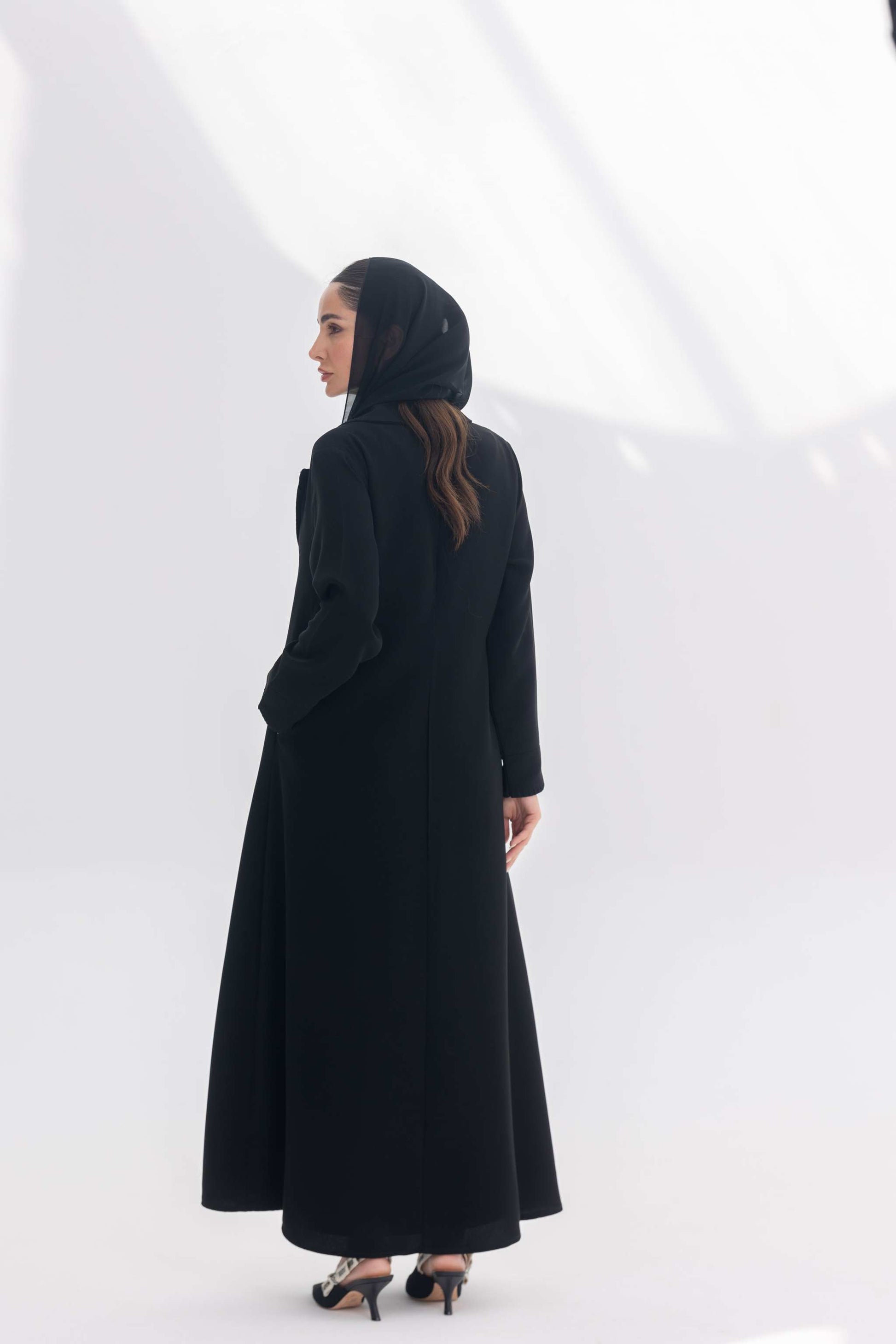 Woman wearing a sophisticated black crepe blazer abaya with intricate embroidery and a tailored silhouette, styled with a black headscarf and heels.